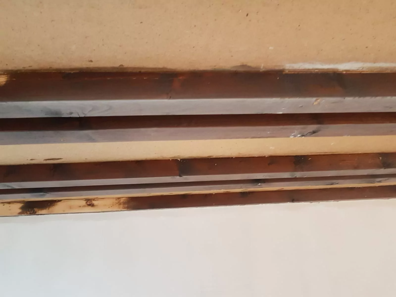 Eine Nahaufnahme einer Decke mit freiliegenden Holzbalken mit Verfärbungen, möglicherweise durch Wasserschäden oder Flecken. Die Balken stehen vor einem hellen Hintergrund.