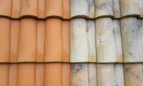 Ein Dach mit zwei Ziegelabschnitten; die linke Seite hat saubere, orangefarbene Ziegel, während die rechte Seite Ziegel mit Anzeichen von Verwitterung und Verfärbung aufweist.